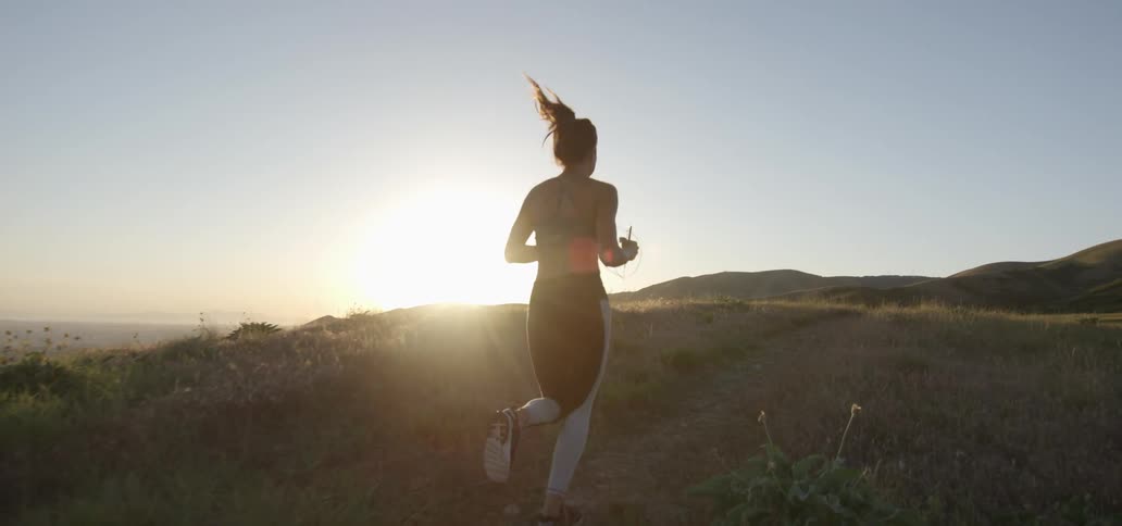 Woman jogs down a grassy path at sunrise