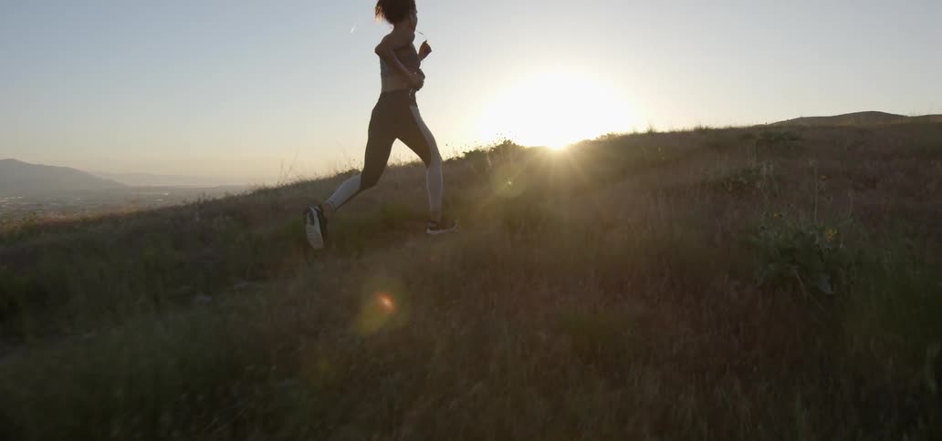 A woman runs up a hill at sunset