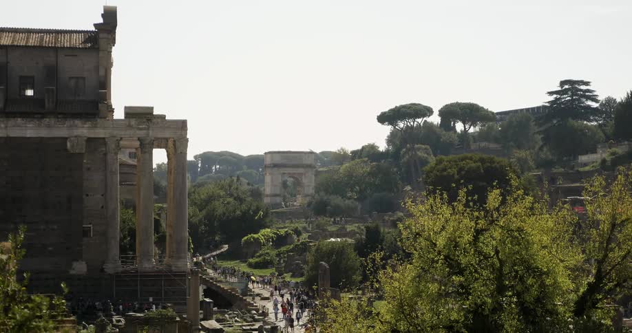 People walking on a sidewalk past ancient ruins