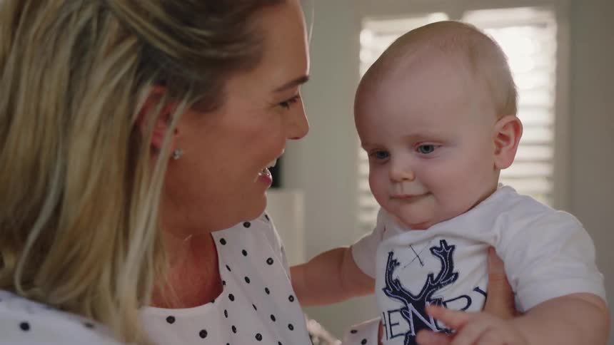 A woman smiles while holding a baby at home
