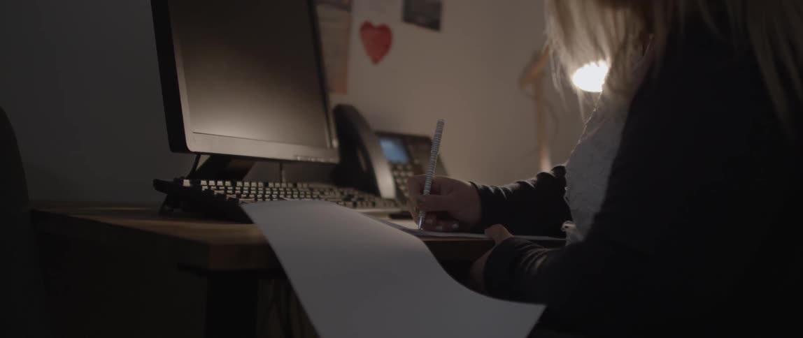 A blonde woman writes on stapled papers