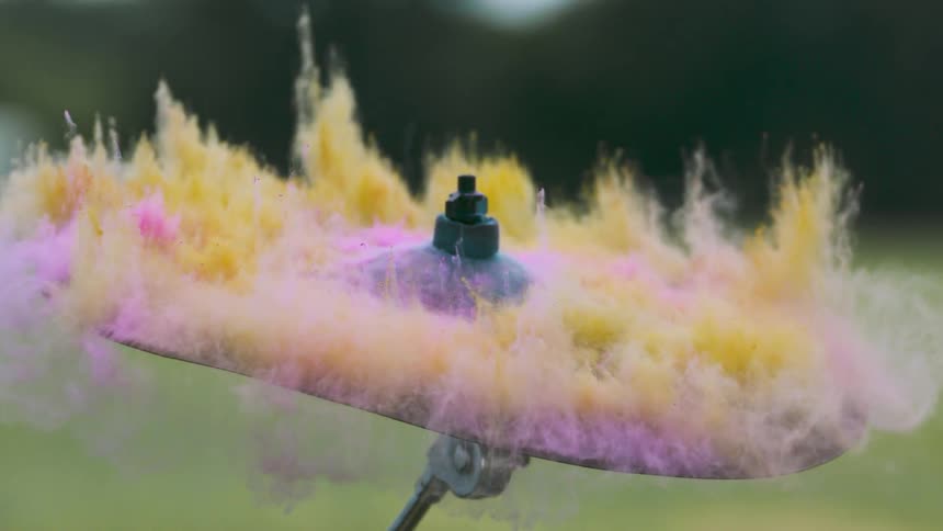A drumstick hits a cymbal that is covered in colorful powder
