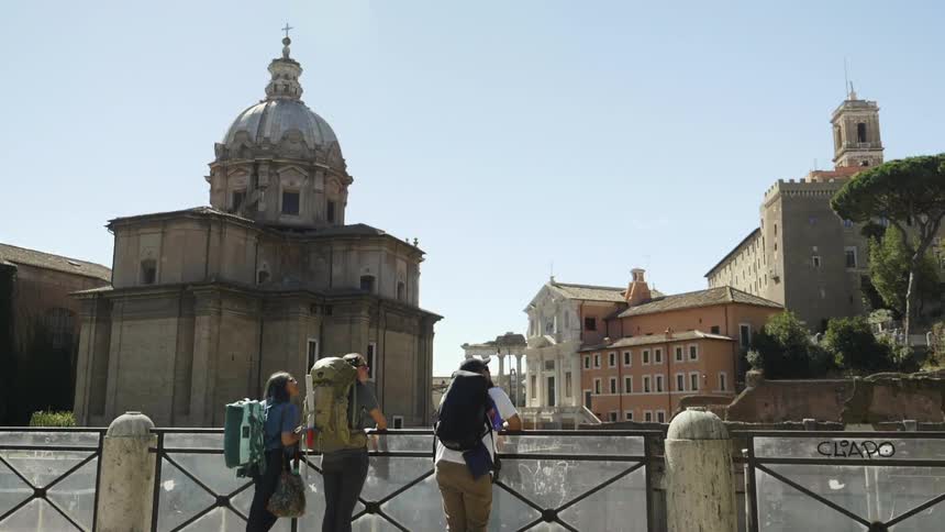 Tourists with backpacks stand overlooking a city with many ruins and old buildings