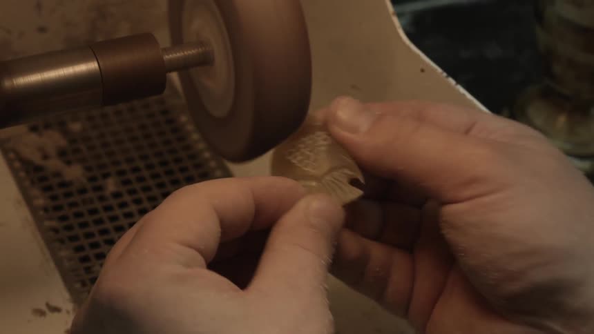 A person grinds down a piece of stone with carvings