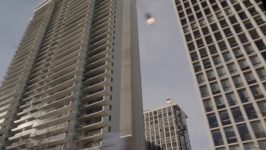 A vehicle drives by tall city buildings on a sunny day