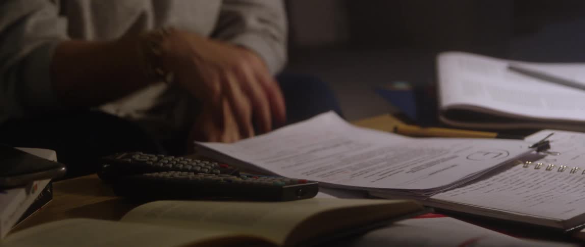 A woman sitting in front of a paper graded f uses a remote control