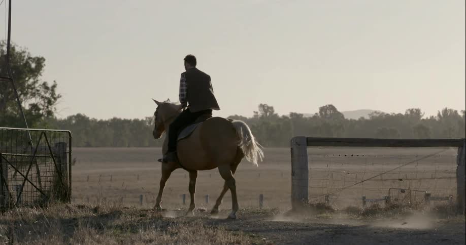 A man rides a horse on a ranch on a sunny day