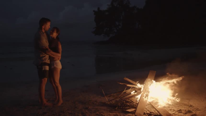 Two people hug near a campfire