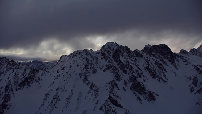 Dark clouds gather over snow covered peaks at sunset