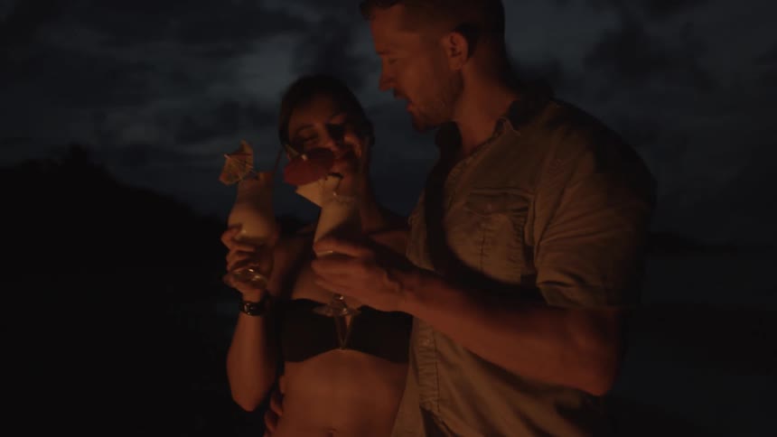 Man and woman drinking beverages on the beach at night