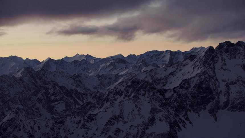 Storm clouds hover over snow-covered mountain peaks at dusk