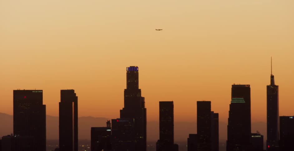 Airplane flying over skyscrapers at sunset