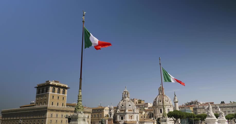 Two flags blow in the wind in front of city buildings