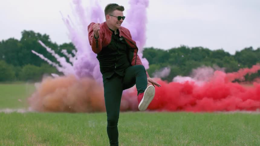 Man jumping into the air as colorful powders explode behind him in a field