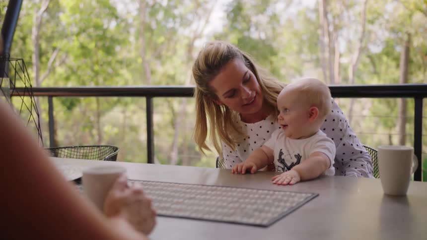 A woman holds a baby at a table on the porch
