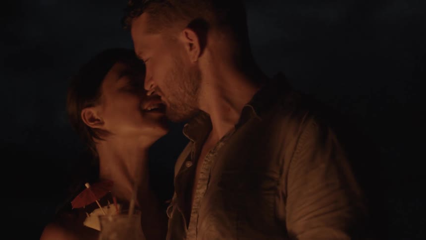 A woman whispers in a man's ear while drinking near a bonfire at night