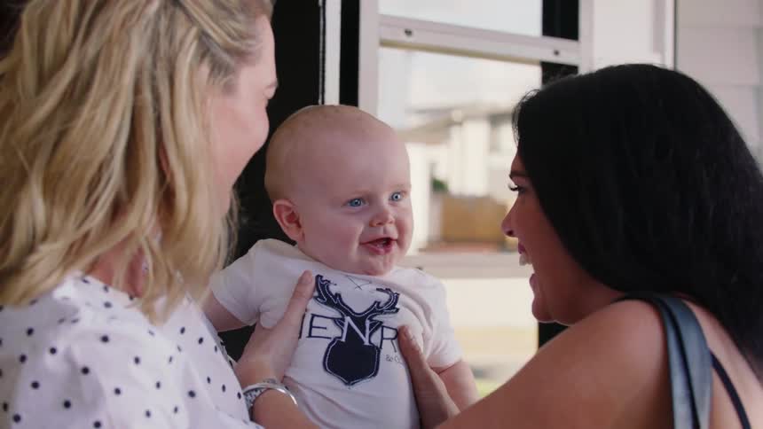 A woman hands off a happy baby who is raised into the air