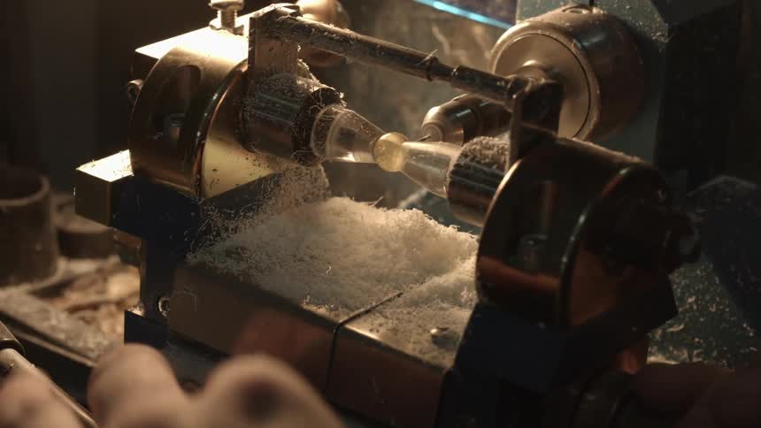 A person uses tools to drill a hole in a bead