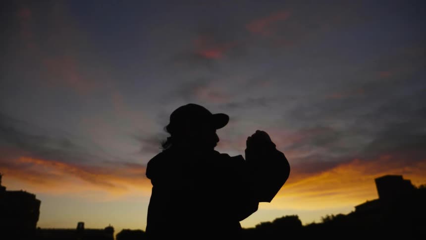 A silhouetted man stands outside at sunset
