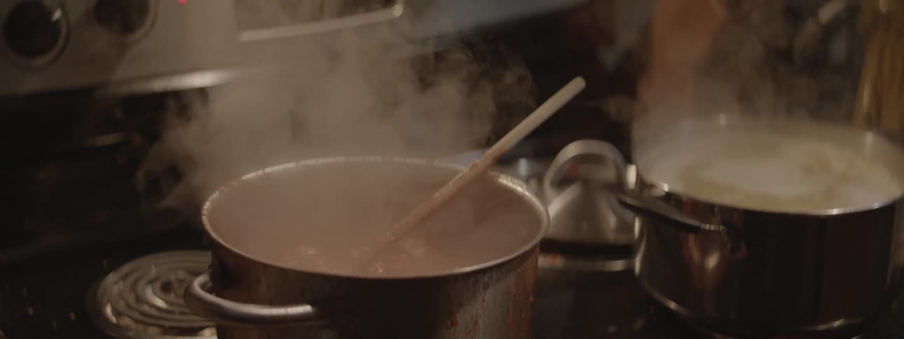 Couple kissing in a kitchen as the man stirs some boiling food on a stove