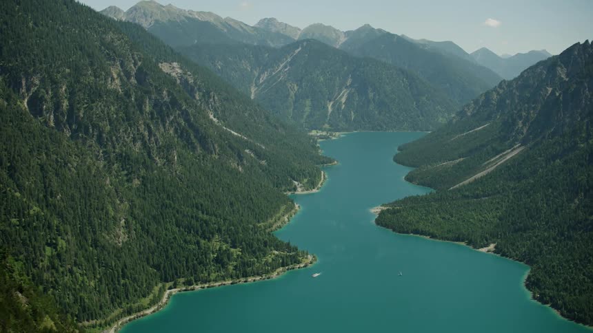 A lake runs through these mountain ranges with light fog at the top