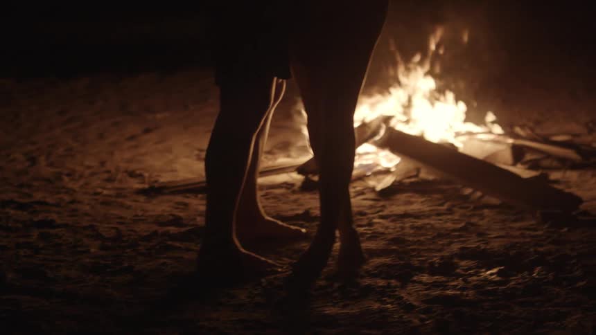 A couple stands near a small fire