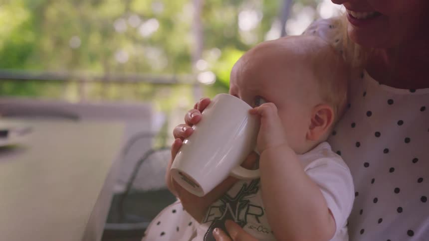 Woman holds a child on her lap letting him drink from a mug
