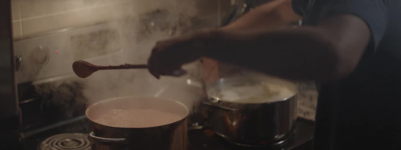 A man and woman kiss then the man runs to stir food in a pot