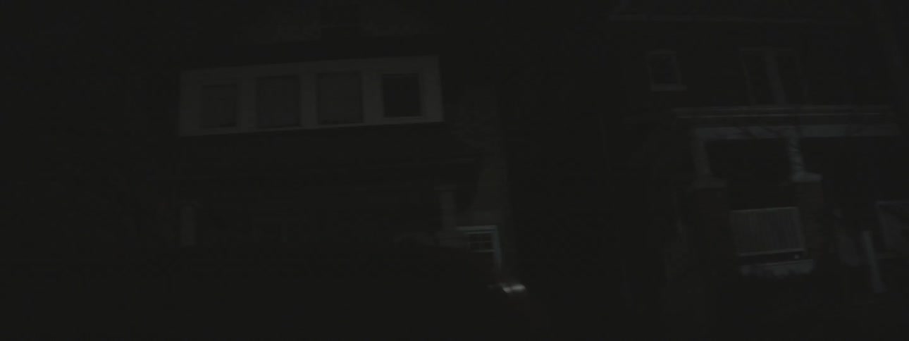 The street is dark with only a few homes with their lights on