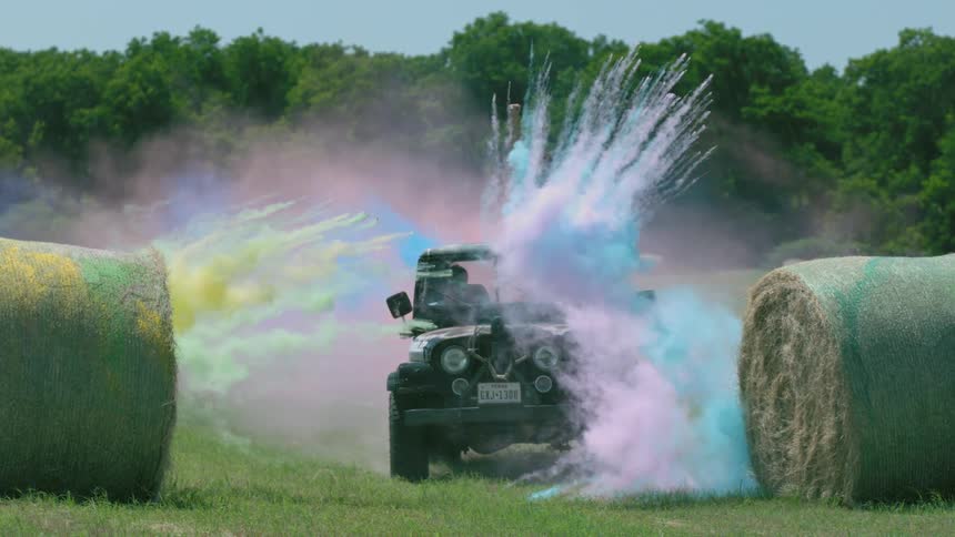 A jeep drives past hay bales as colored powder explodes