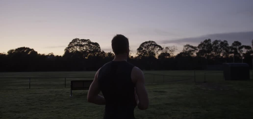 An man carrying  a rugby ball walks toward a field at dusk