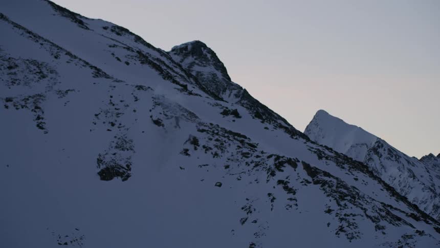 An avalanche of snow falls off the side of the mountain