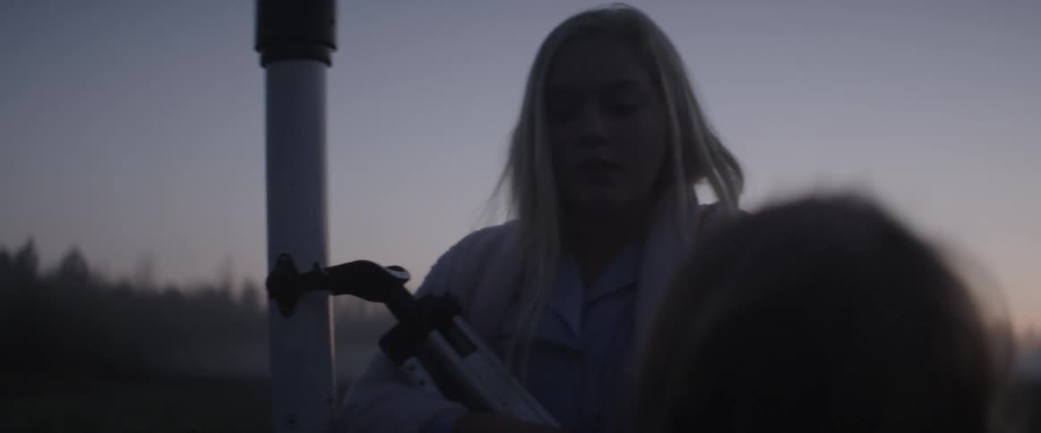 Two girls are walking on a field carrying a telescope