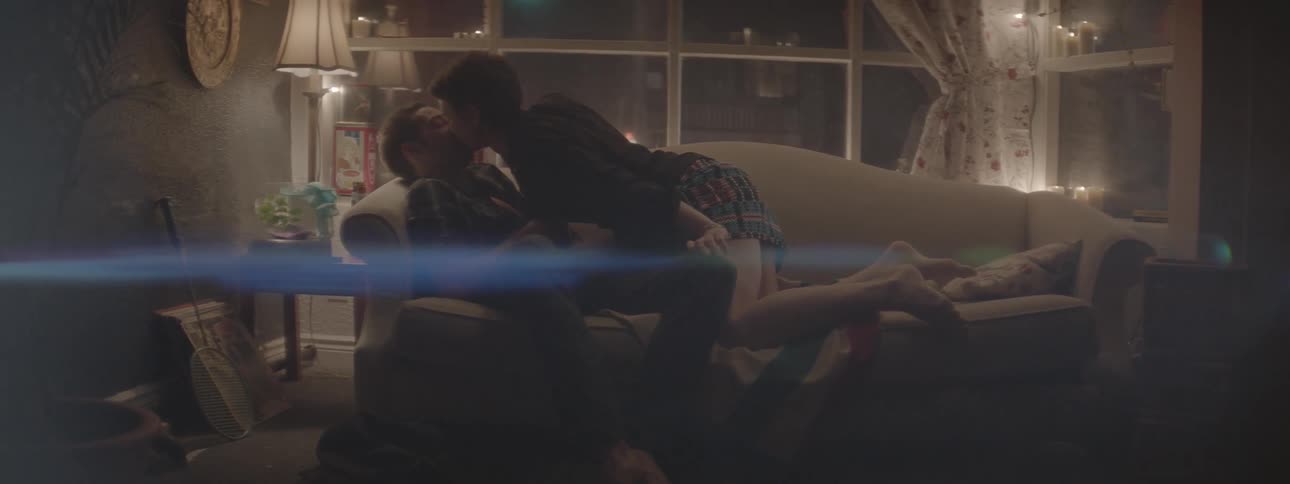 A woman leans over on the couch and kisses a man