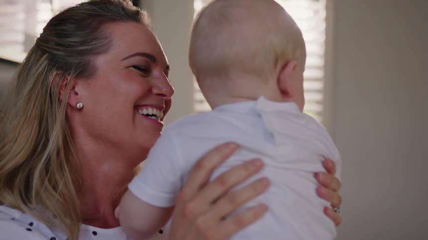 A woman smiles while holding a baby at home