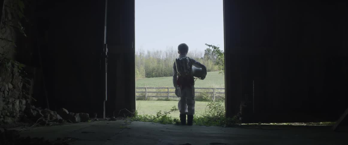 Little boy wearing astronaut costume holding helmet in barn doorway