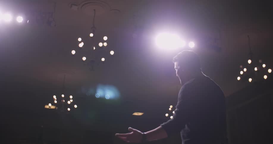 Man stands on a stage reading a book out loud