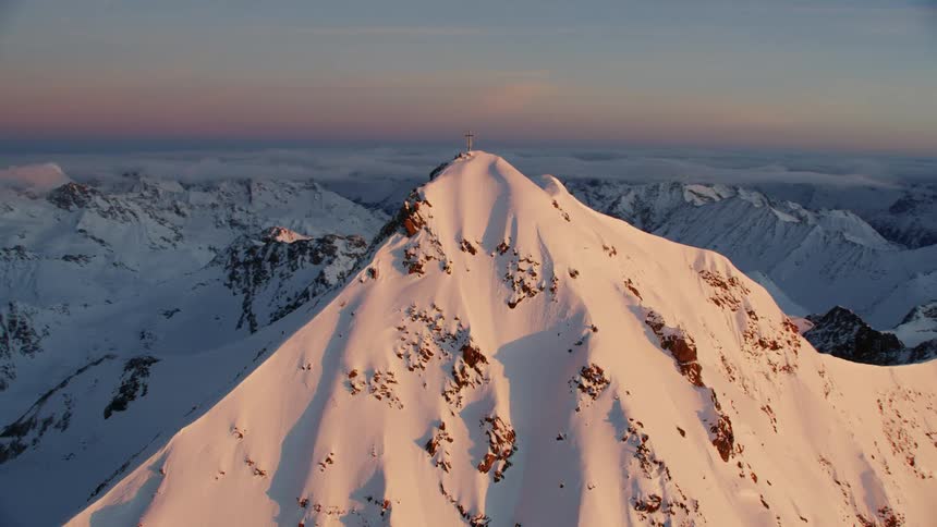 Cross on top of snowy mountain at sunset