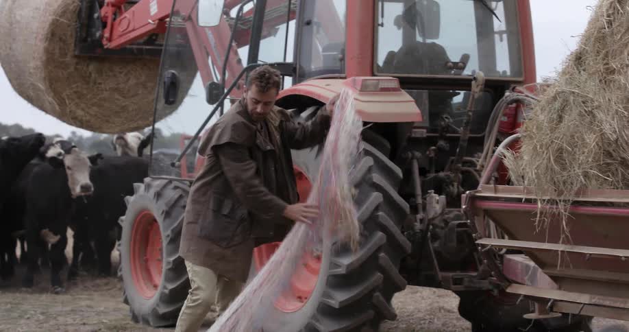 Man takes netting off of hay bales on a tractor