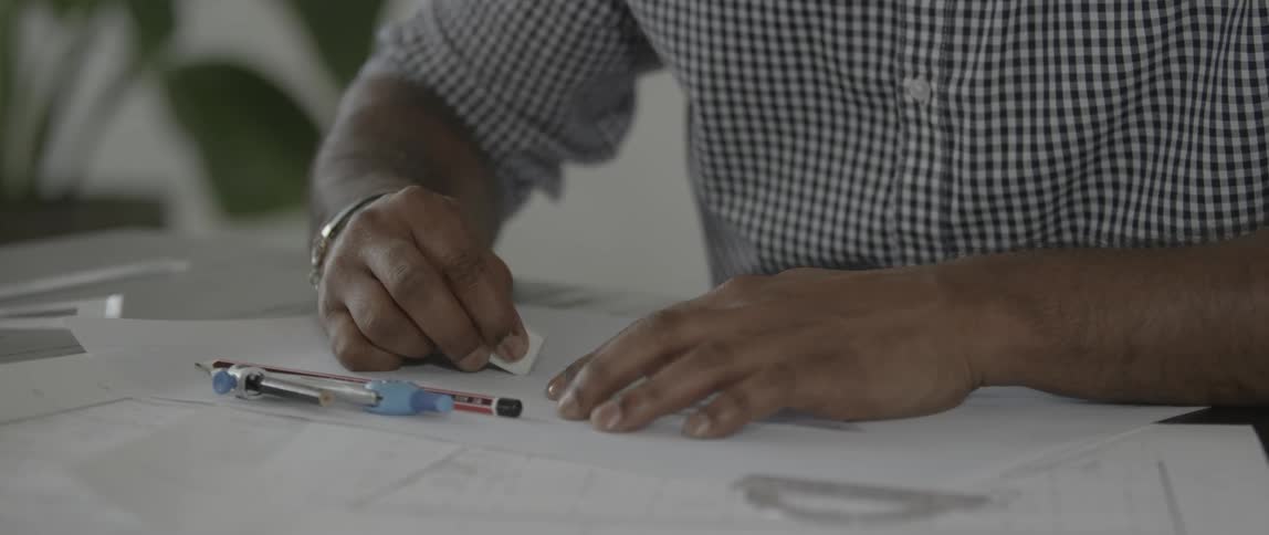 A man erases a mark on a plan then picks up a pencil