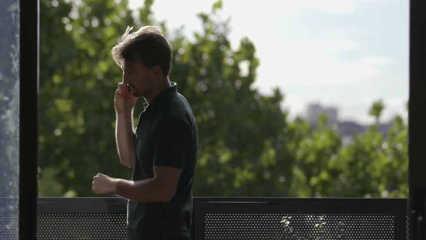 A man stands on a balcony while talking on the phone