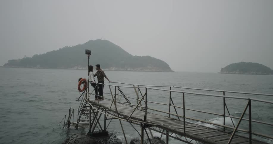 Man and woman kissing on dock over ocean water on overcast day