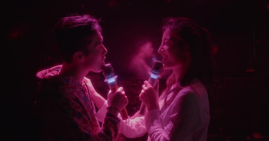 A couple sing and dance together in a dark room