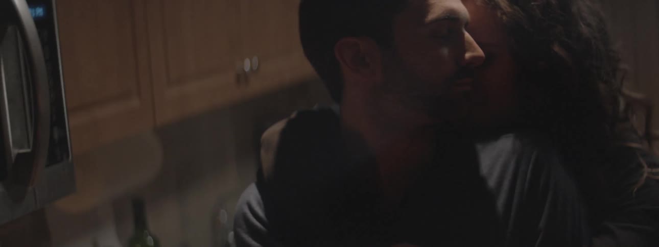 A woman leans over a man kissing him