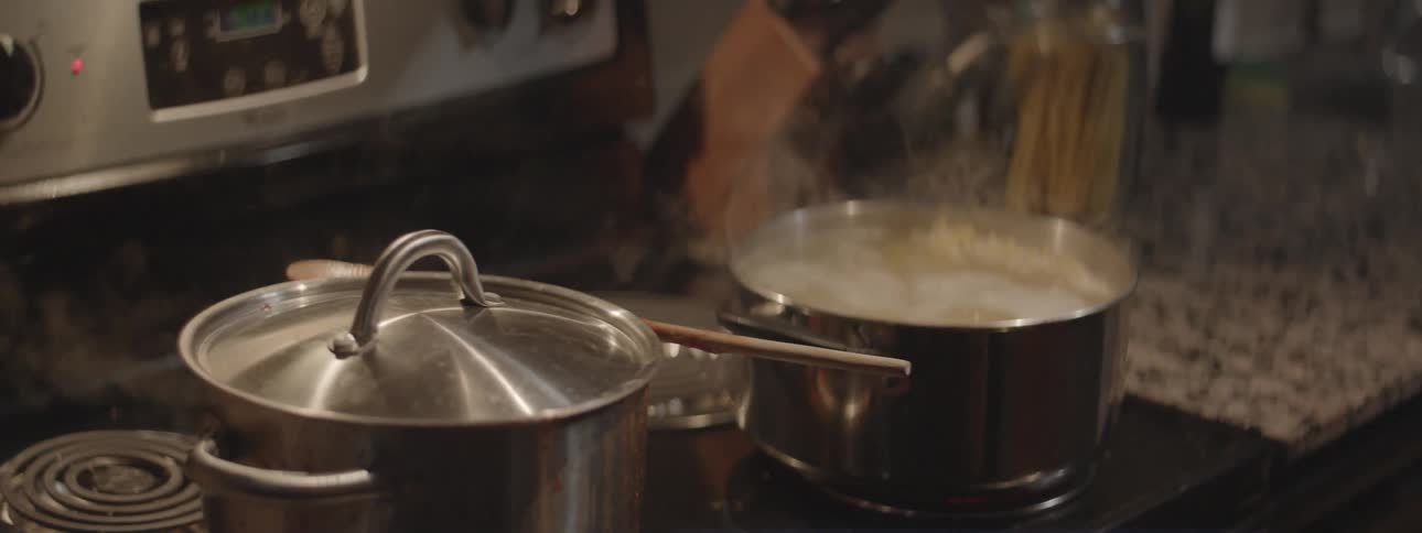 Man places a lid on some boiling food next to another steaming pot on a stove