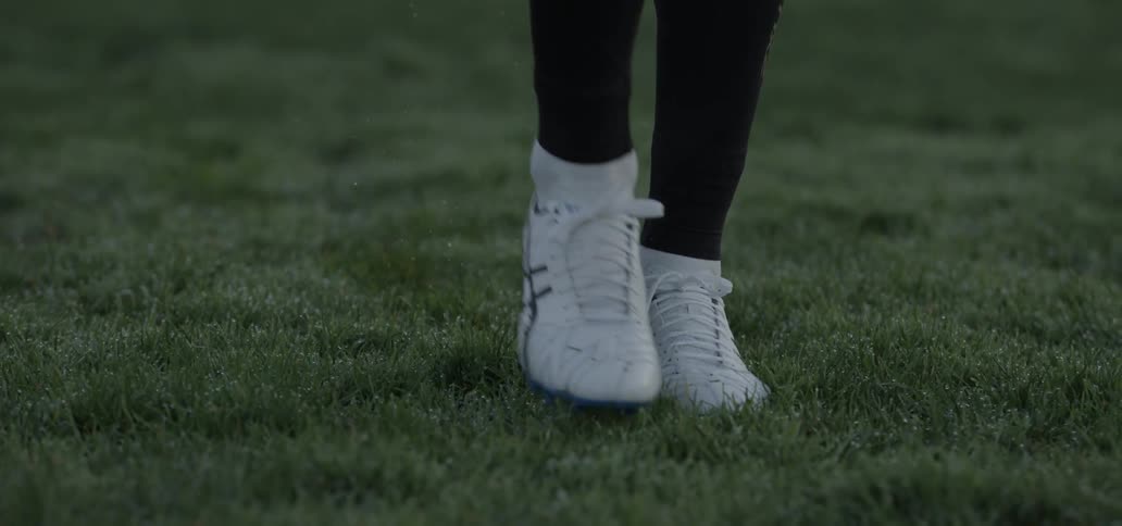 A person wearing sneakers walks on grass turf