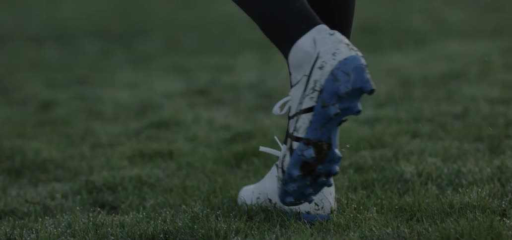 Person wearing cleats walking on a grassy field