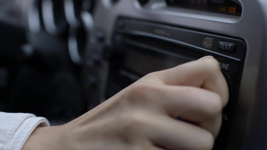 A woman changes the car radio channel and turns up the volume
