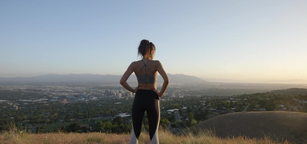 A woman looks over a valley with city buildings below