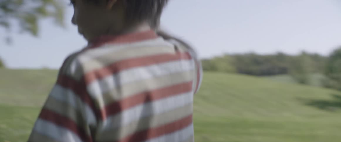 A boy runs outside with a toy on a sunny day